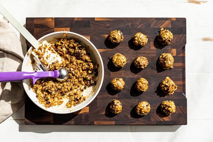 Using a cookie scoop to portion out the energy bites on a wooden cutting board.
