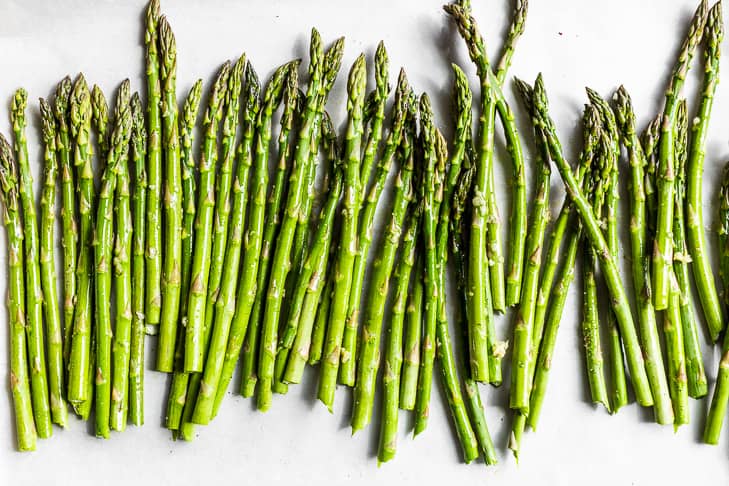 The asparagus tossed together with the olive oil, garlic, and sea salt on parchment paper.