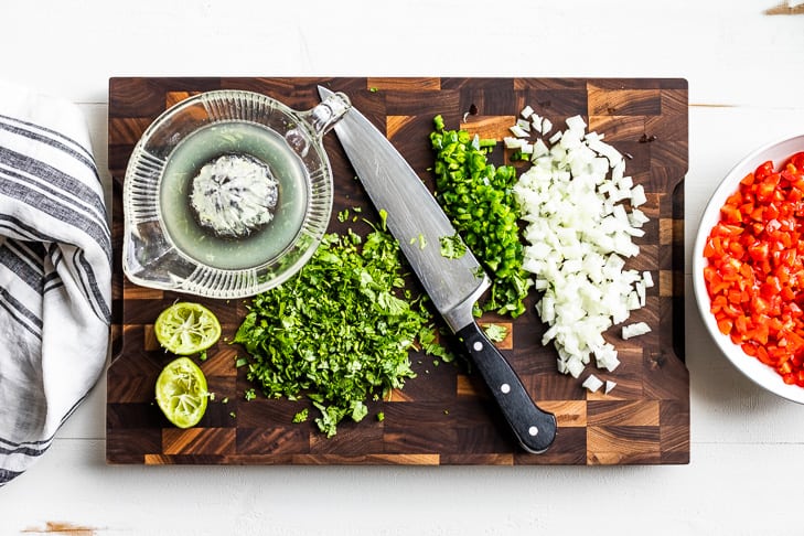 Minced cilantro, jalapeno, and onion with freshly squeezed lime juice prepped on a wooden cutting board.