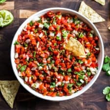 A white bowl filled with Pico de Gallo with corn chips and cilantro around it.
