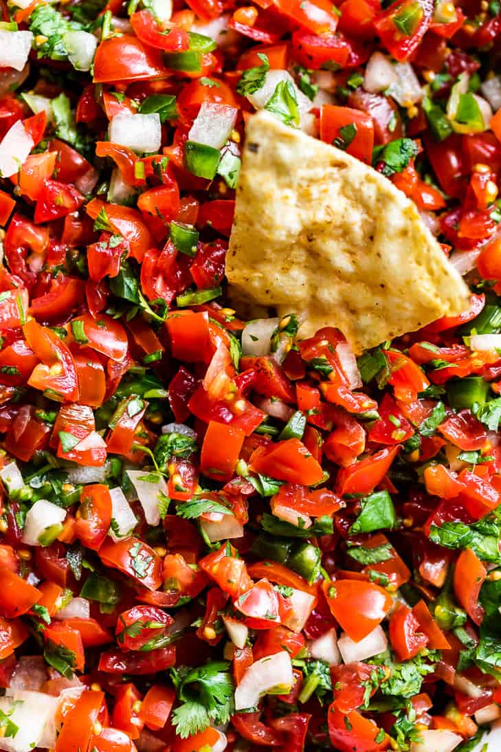 A up close view of Pico de Gallo with a chip being dipped into it.