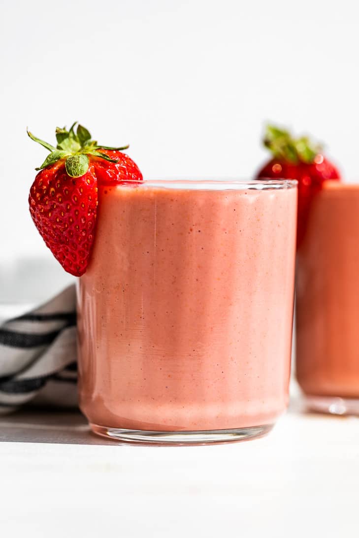 Two glasses of Strawberry Banana Smoothie with strawberries on the side of the glasses.