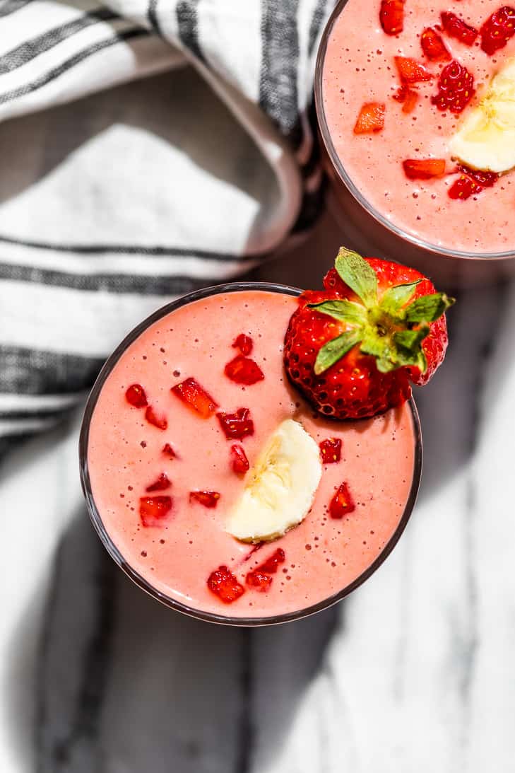 Straight down view of two glasses Strawberry Smoothie topped with banana slices and diced strawberries.