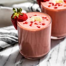 Two glasses of Strawberry Banana Smoothie topped with banana sliced and diced strawberries with a strawberry on the side of each glass.