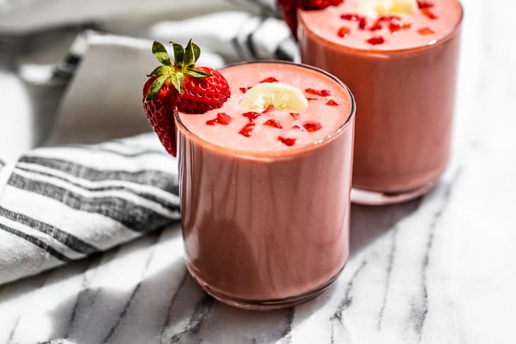 Two glasses of Strawberry Banana Smoothie topped with banana sliced and diced strawberries with a strawberry on the side of each glass.