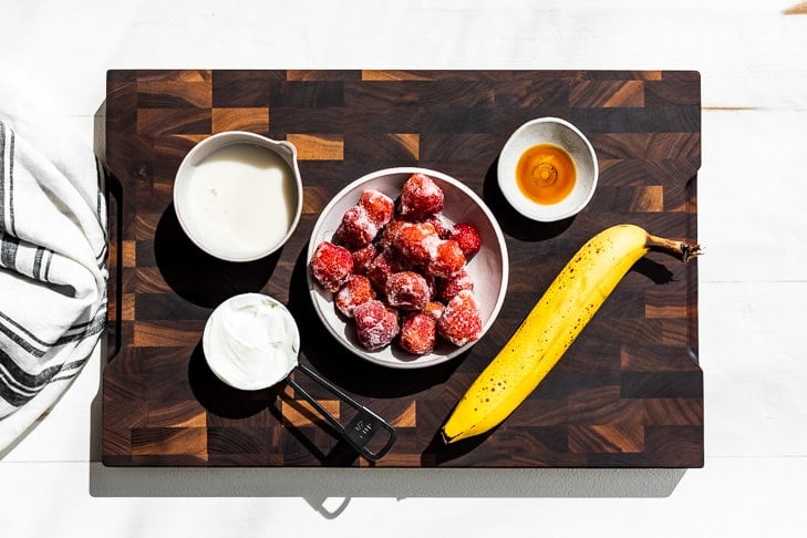 All the ingredients for the smoothie measured out and on a wooden cutting board.