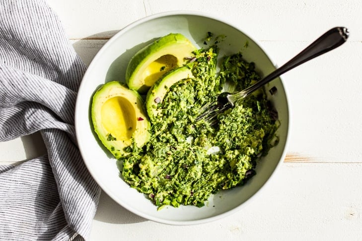 Mashing the chopped cilantro, onion, and jalapeno into the avocados.