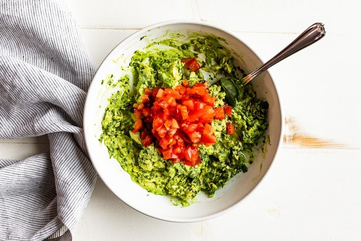 Adding the optional tomatoes to the finished guacamole.