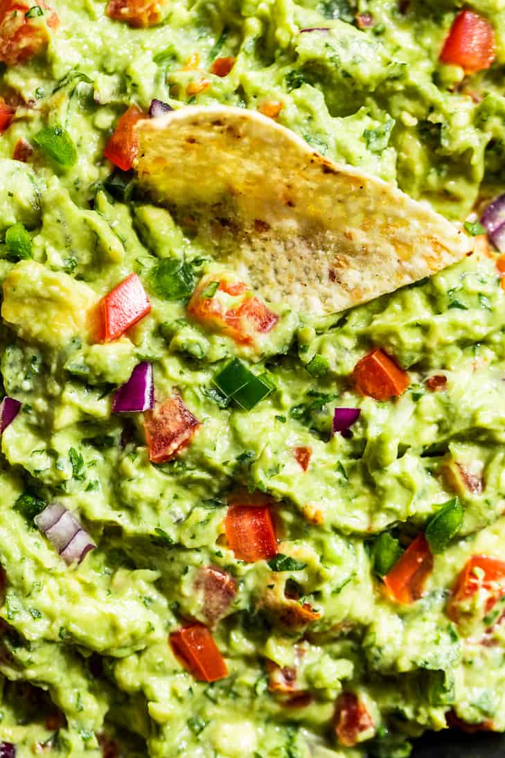Close up view of guacamole with a chip being dipped in.