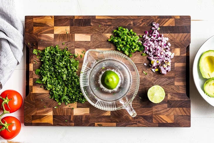 Minced cliantro, onion, jalapeno, and lime juice prepped for the guacamole on a wooden cutting board.