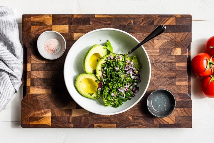 Avocados added to the bowl topped with the minced cilantro, jalapeno, and onion.