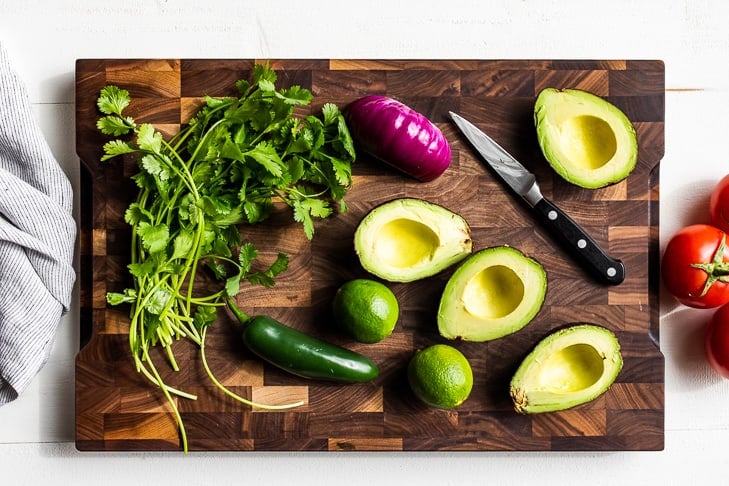 All the ingredients for guacamole on a wooden cutting board.