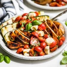 Balsamic Grilled Chicken topped with Caprese Salad on a pottery plate with basil sprigs around it.