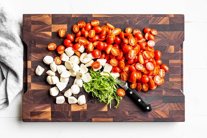Cut up tomatoes and mozzarella with sliced basil on a wooden cutting board.