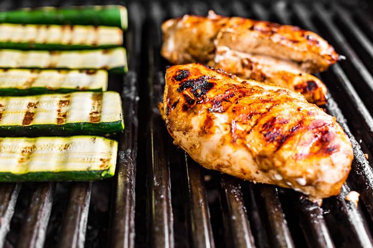Balsamic marinated chicken and zucchini turned over on the grill with grill marks.