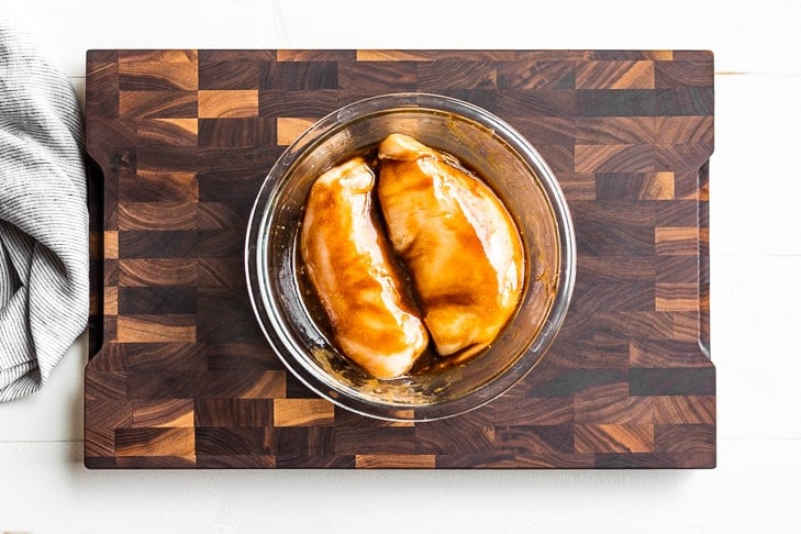 Marinating Balsamic Chicken in a glass bowl on a wooden cutting board.