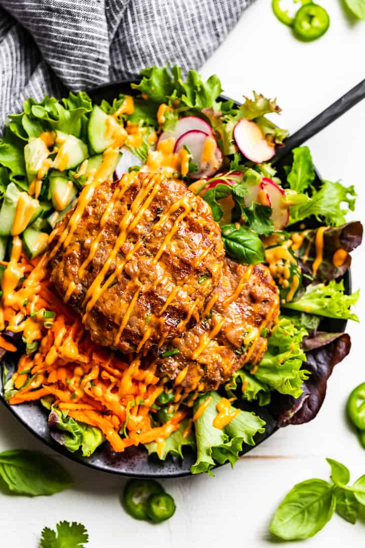 A straight down view of the assembled Banh Mi Burger Bowl on a white background with basil and jalapeno slices around it.