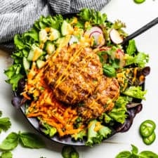 Banh Mi Burger Bowls assembled in a black bowl on a white background with herbs around it and a blue linen napkin in the background.