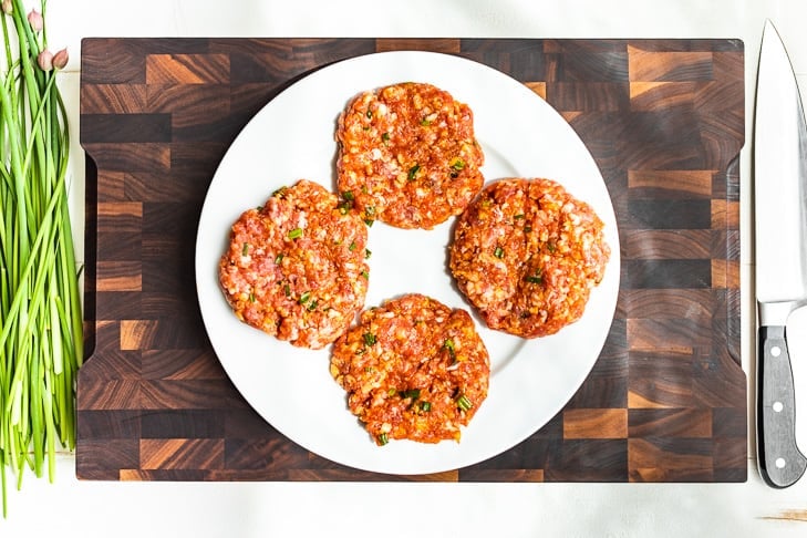 Banh Mi burgers formed on a white plate on a wooden cutting board.