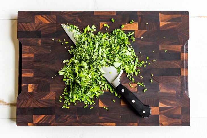 Chopped fresh herbs on a wooden cutting board.