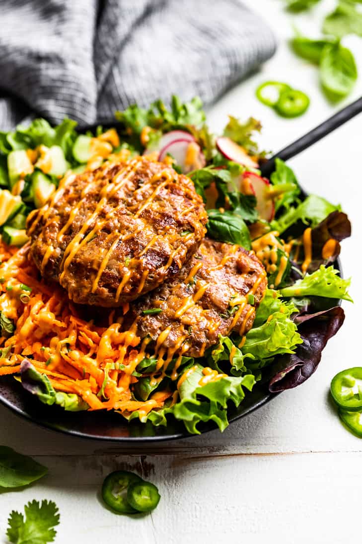 A side view of Banh Mi Burger Bowls assembled in a black bowl on a white background with a blue linen behind the bowl.