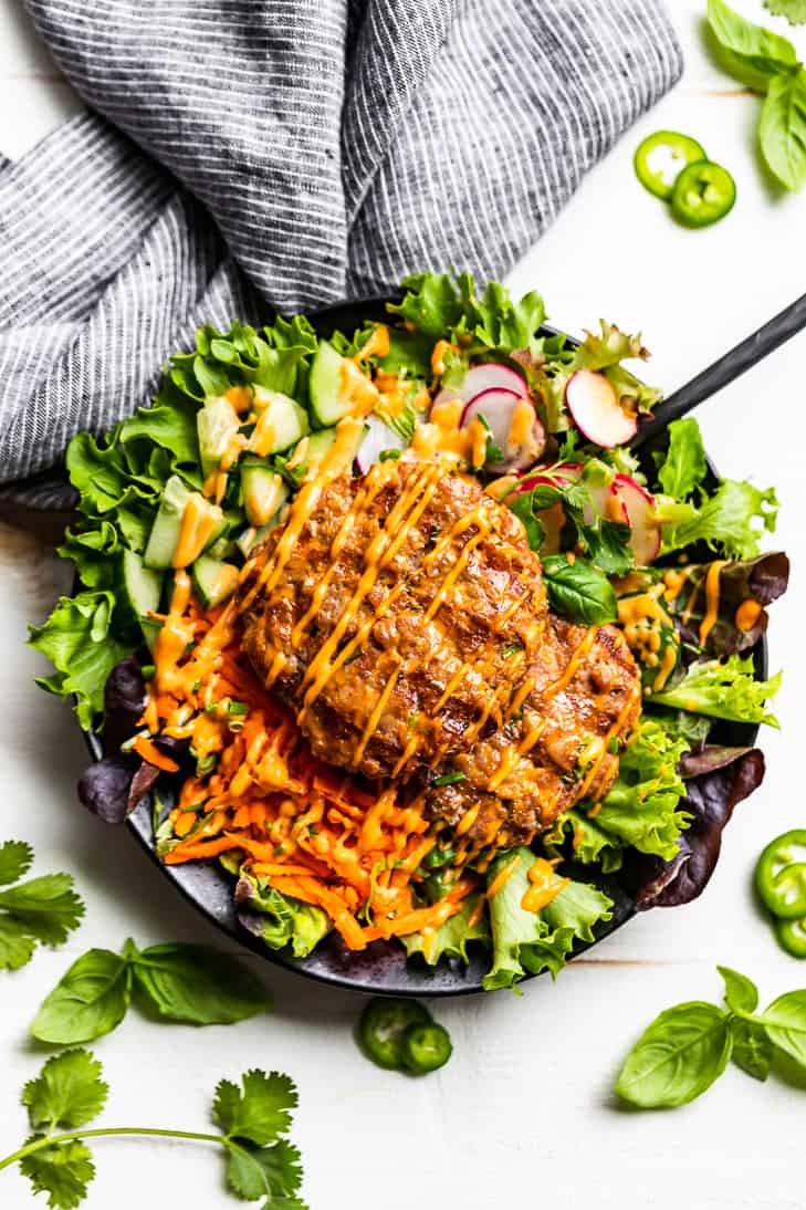 Banh Mi Burger Bowl in a black bowl on a white background with fresh herbs.