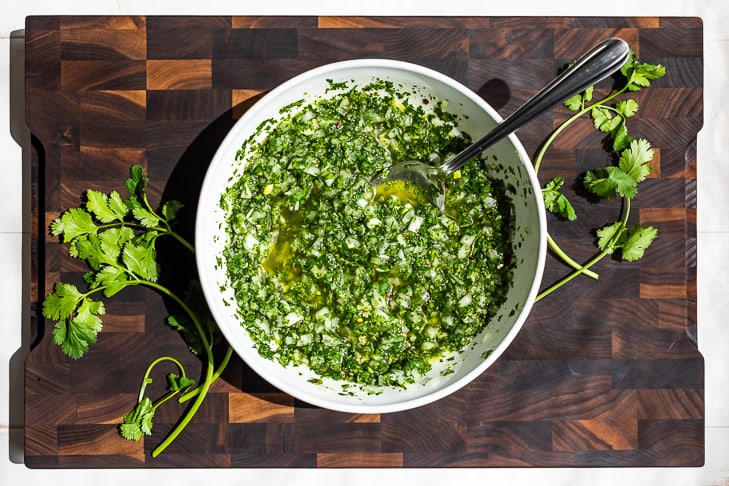 Cilantro Chimichurri stirred together in a white pottery bowl on a wooden cutting board.