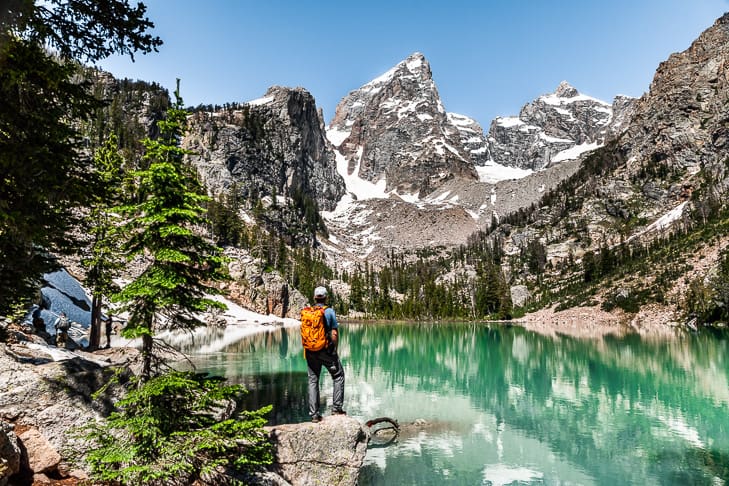 Hiker standing on a rock overlooking Delta Lake with the mountain peaks in the distance.