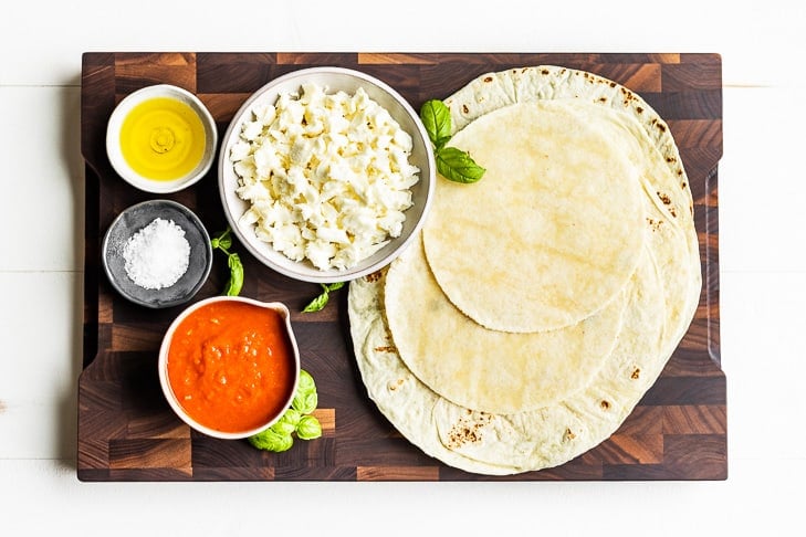 All the ingredients for the Grilled Tortilla Pizzas on a wooden cutting board.