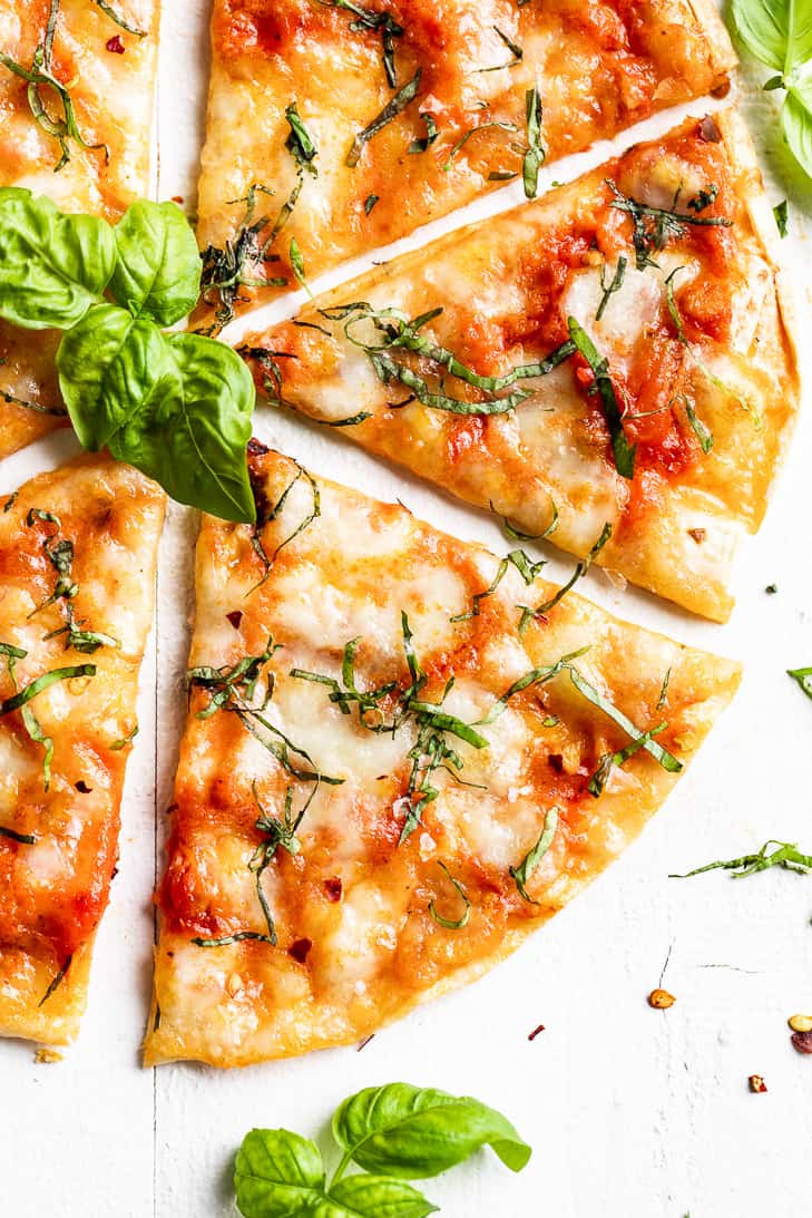 Straight down view of Grilled Tortilla Pizza Margherita sliced up with basil leave around it.