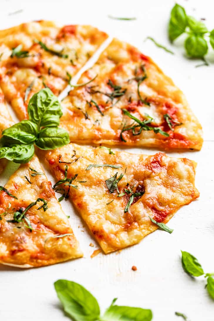 A side view of sliced Grilled Tortilla Pizza Margherita with basil leaves around it.