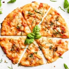 A straight down view of Grilled Tortilla Pizza Margherita sliced with basil leaves around it.