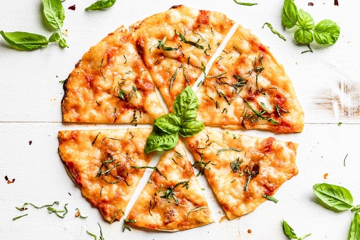 A straight down view of Grilled Tortilla Pizza Margherita sliced with basil leaves around it.