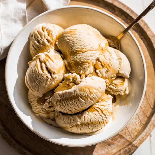 Maple Ice Cream in a cream bowl on a round wooden cutting board with maple syrup drizzled over the top.