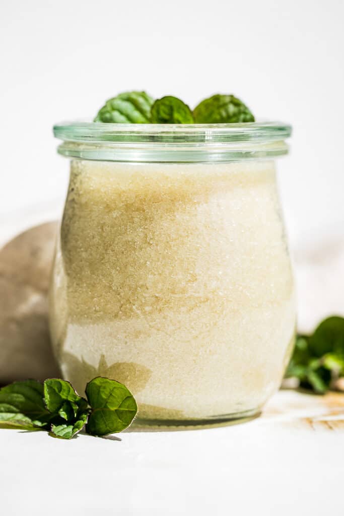 Peppermint Sugar Scrub in a weck green glass jar with mint sprigs on top and mint around it.