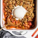 A straight down view of Strawberry Rhubarb Crisp in a white baking dish with a large scoop of coconut ice cream on top.