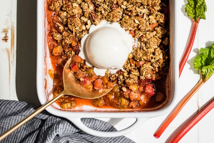 A straight down view of Strawberry Rhubarb Crisp in a white baking dish with a large scoop of coconut ice cream on top.