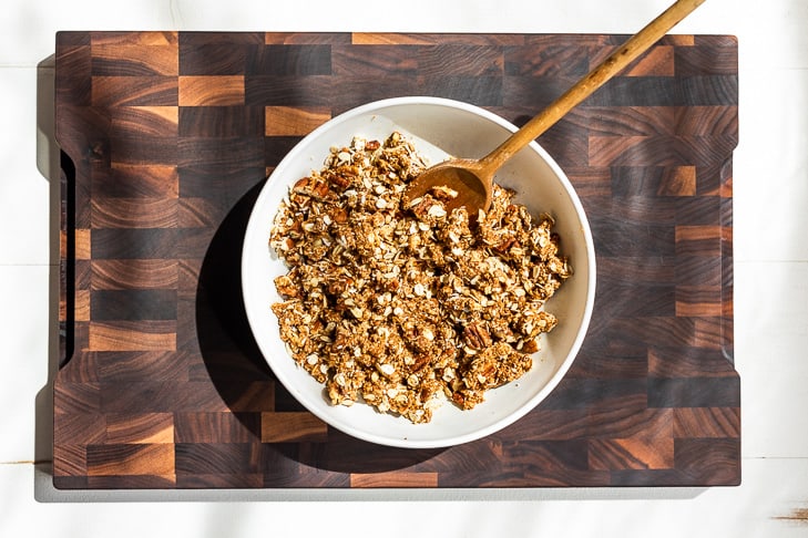 The crisp topping mixed up in a white bowl with a wooden spoon on the wooden cutting board.