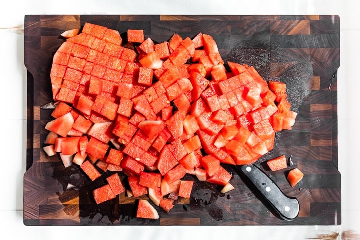 Cubed up watermelon on a wooden cutting board.