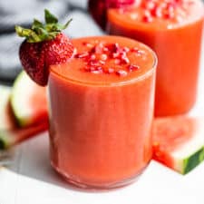 Two glasses of Strawberry Watermelon Smoothie on a white background with small cubes of watermelon on top and a strawberry on the side of the glass.