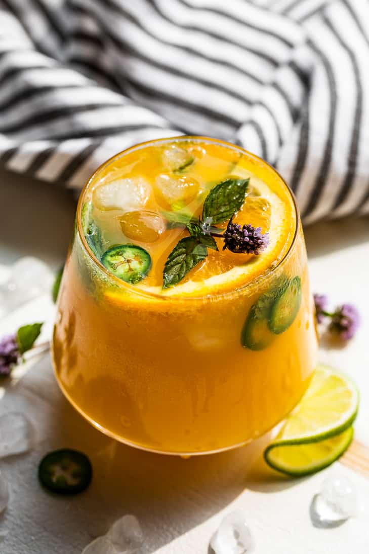 Mango Orange Kombucha Mocktail in a cocktail glass topped with jalapeno slices, mint, and a sliced orange.