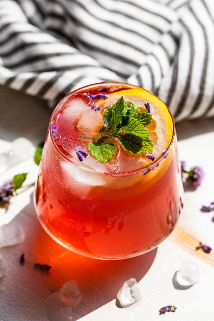 A cocktail glass with a pink Kombucha Mocktail topped with ice, mint, and a slice of lemon.