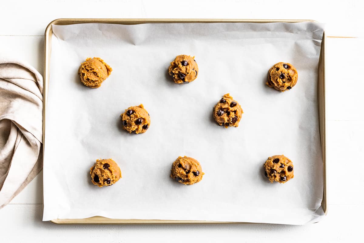 Scoops of cookie dough on a parchment lined baking sheet.