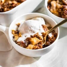 Two bowls of Apple Crisp with the baking dish in the background.