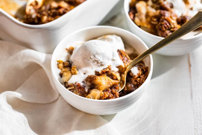 Two bowls of Apple Crisp with the baking dish in the background.