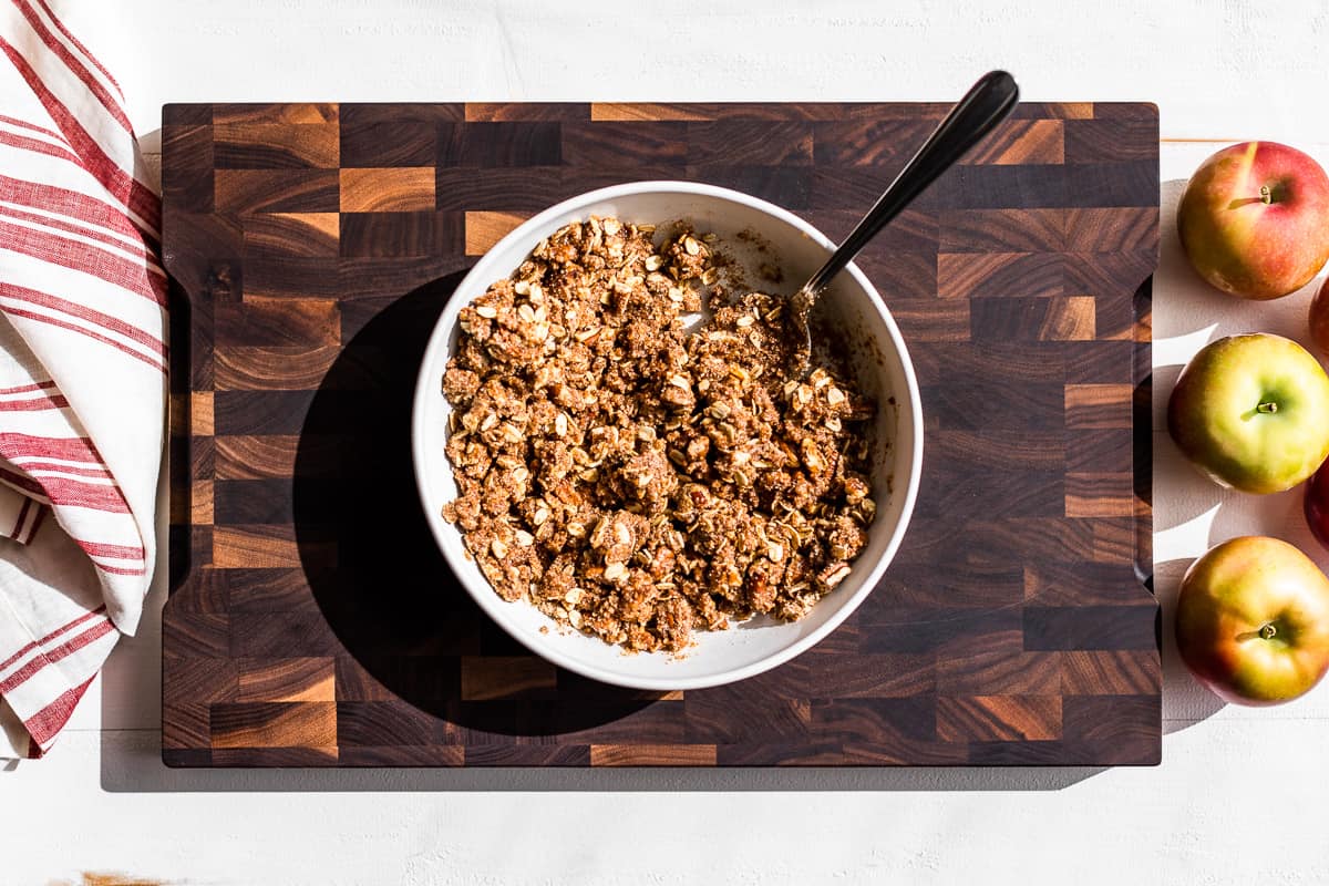 Crisp topping mixed together in a white bowl on a wooden cutting board.