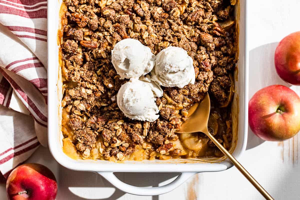 Finished apple crisp topped with ice cream with a golden spoon on the side.