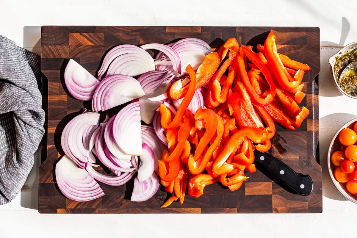 Cut up onions and peppers on a wooden cutting board.