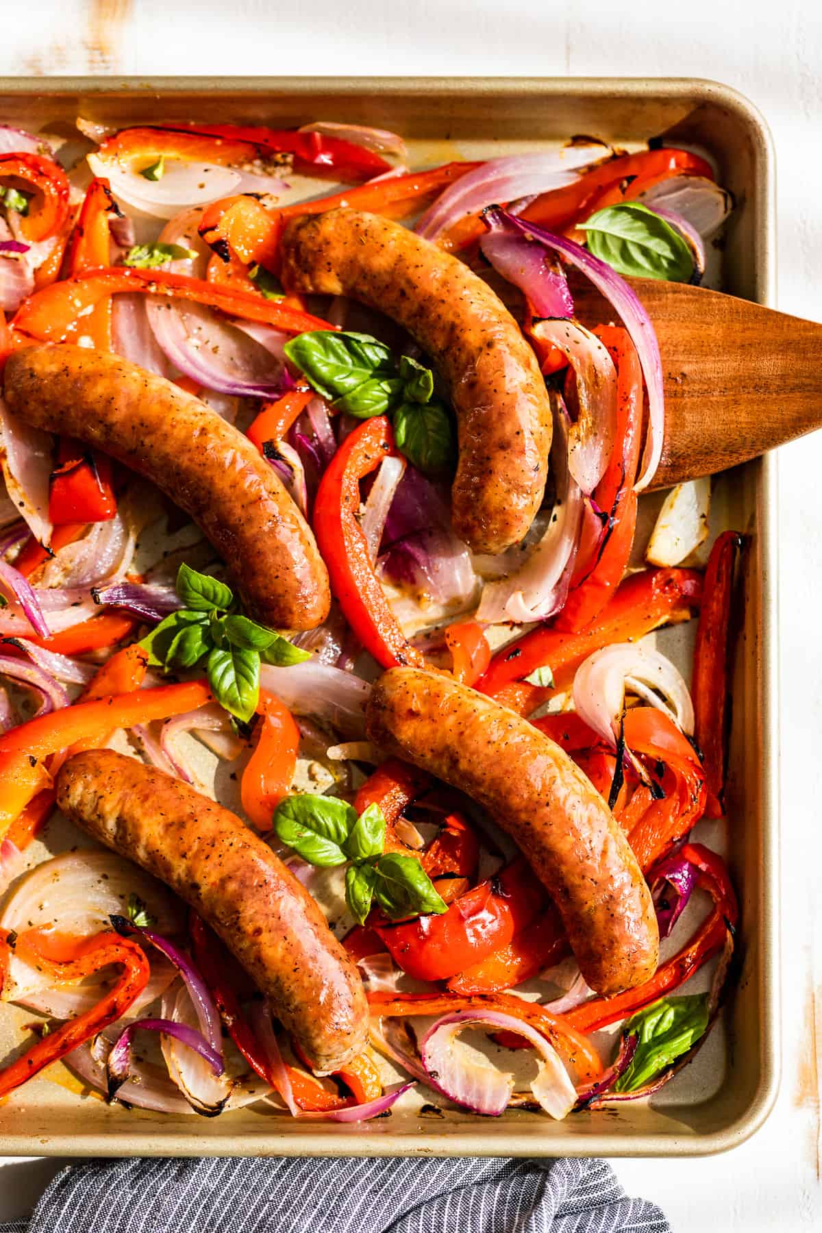 Sausage with peppers and onions and basil on a cookie sheet.