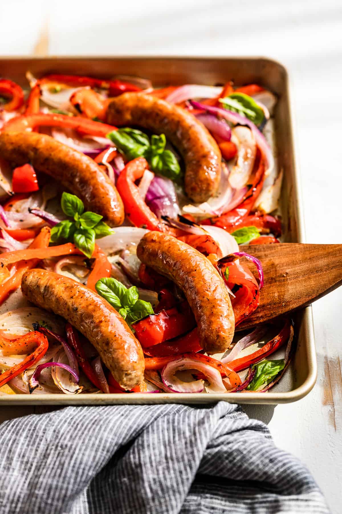 Closer side view of sausage and peppers with a wooden spatula.